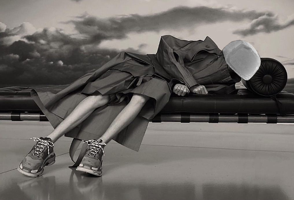 boy in duster coat and sneakers laying on cushioned bench